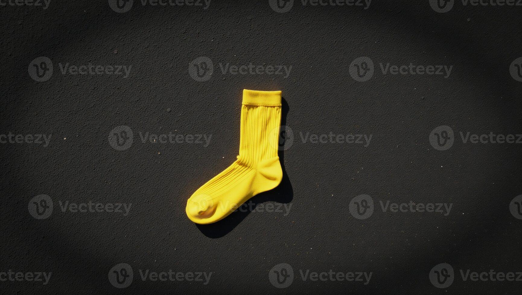 A lone yellow sock rests on a gritty weathered ground photo