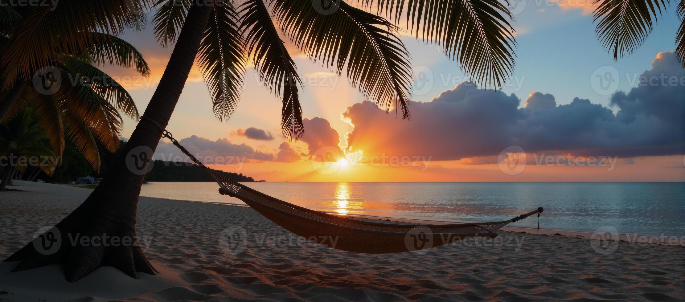 Beach scene featuring silhouetted hammock under palms during sunset photo
