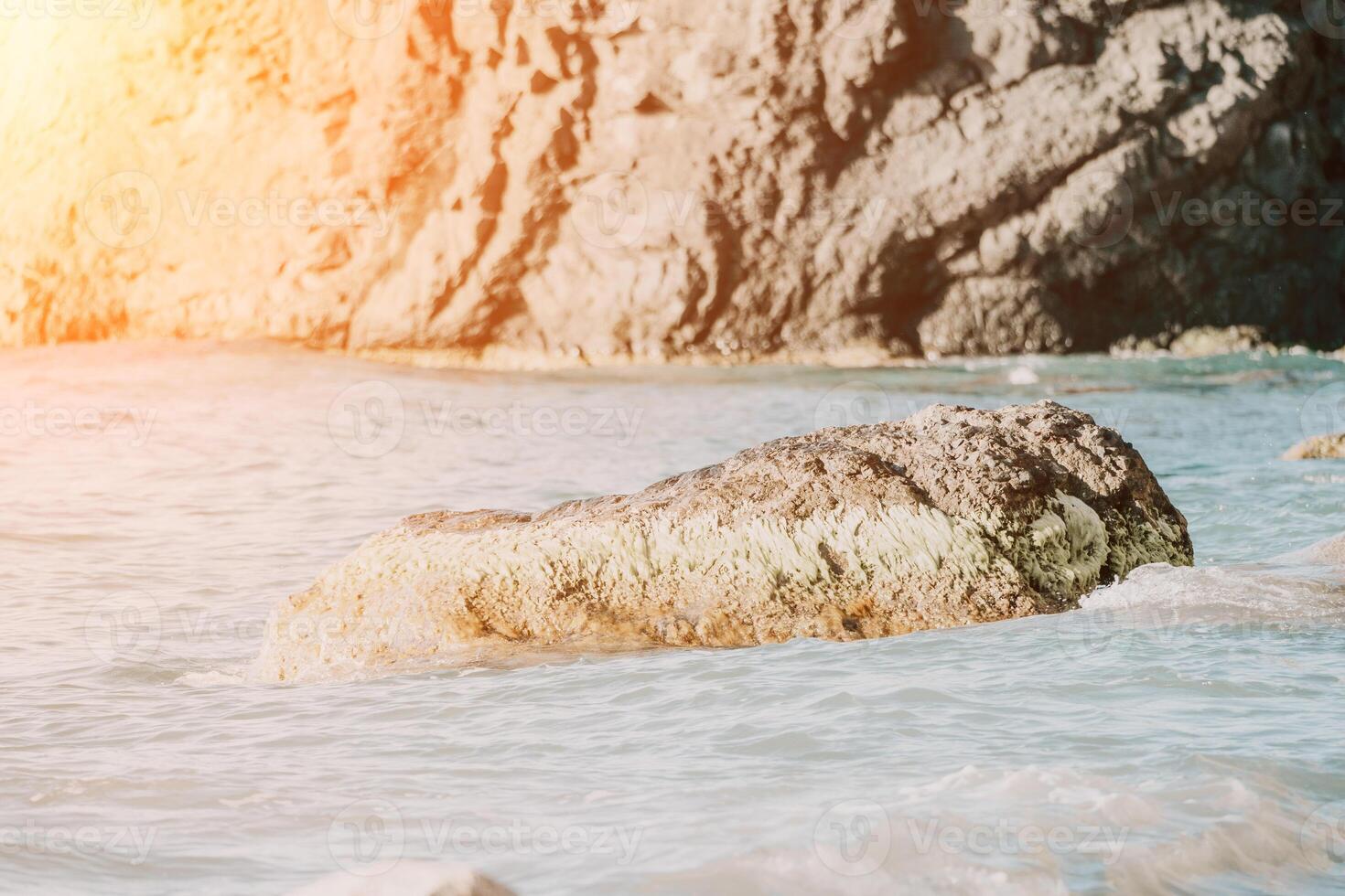 A red burning sunset over the sea with rocky volcanic cliff. Abstract nature summer ocean sea background. Small waves on golden warm water surface with bokeh lights from sun. photo