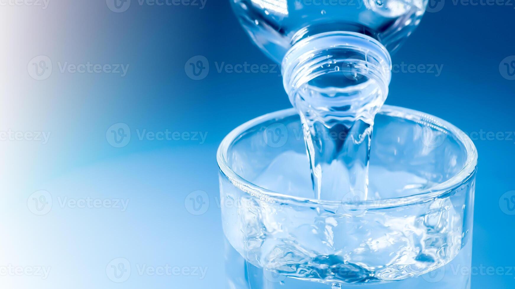 Crystal Clear Water Pouring from Bottle into Glass on Blue Background with Refreshing Splash photo