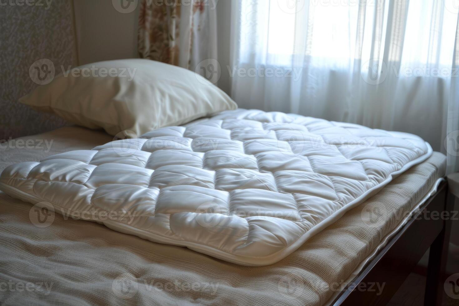 White mattress pad lying on top of bed with pillow behind photo
