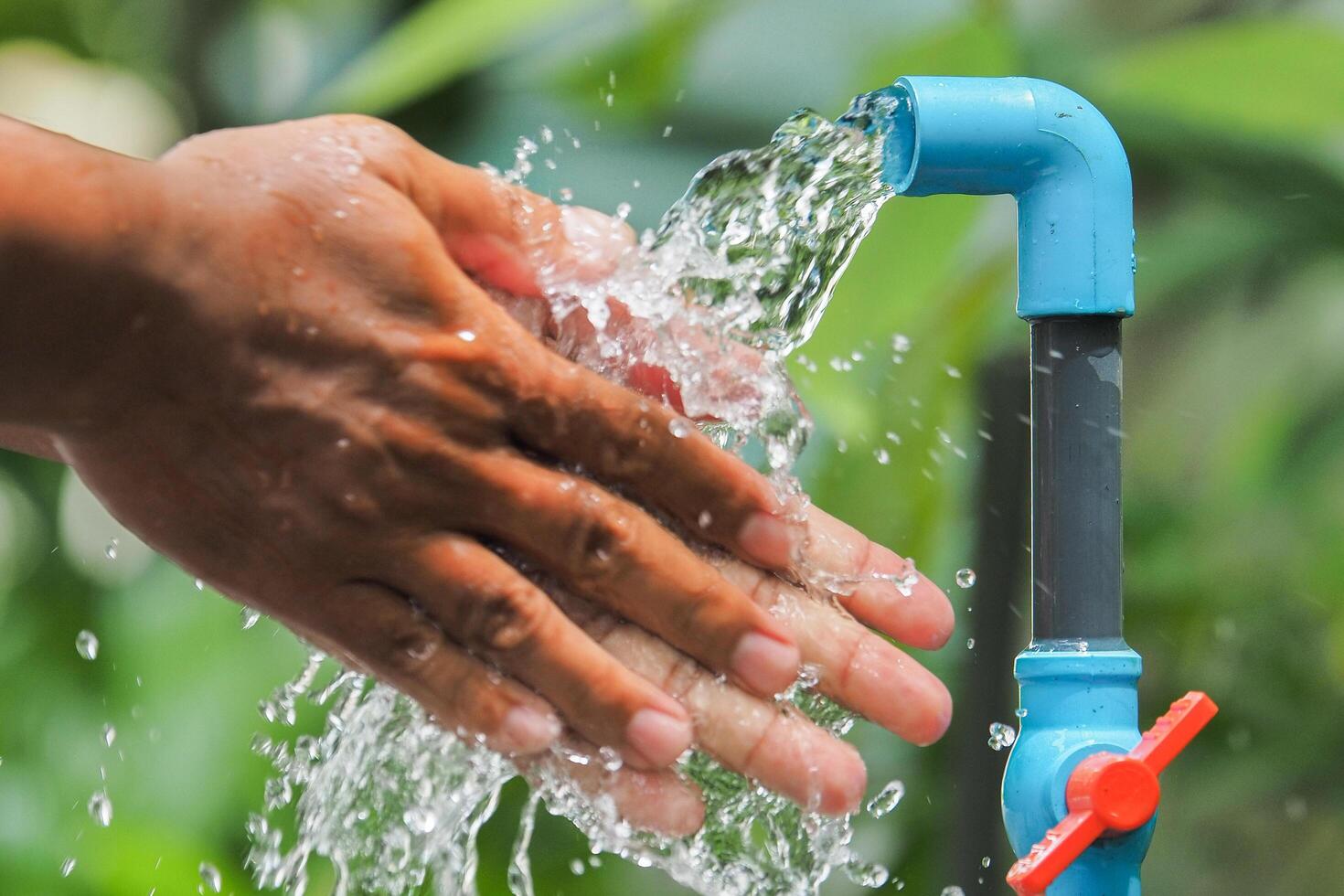 Hands Being Washed Under Running Water from a Blue Outdoor Faucet in a Garden Setting photo