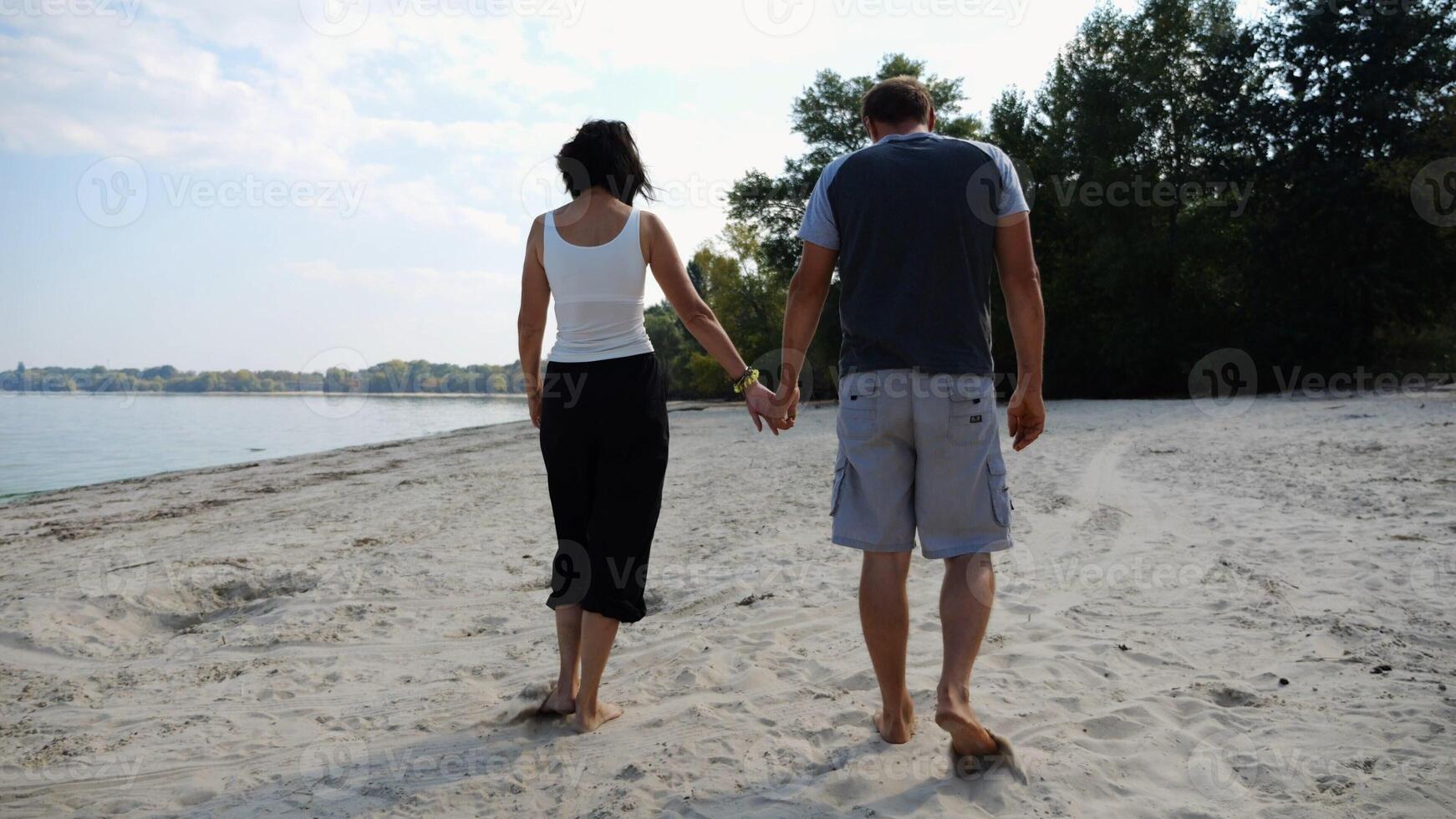 Couple holding hands of each other and walking at coast. Happy pair going along seashore at sunny day. Lovers spending time together at resort. Concept of vacation or holiday. Slow mo photo