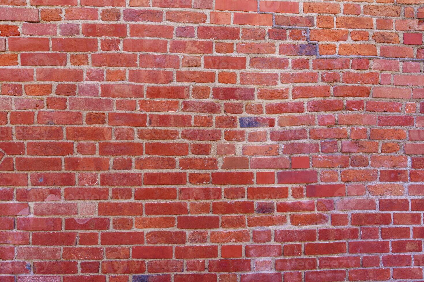 This high-quality photo showcases a red brick wall with a rough texture, featuring various shades from light to dark red. Cracks and chips add character, making it ideal for backgrounds.