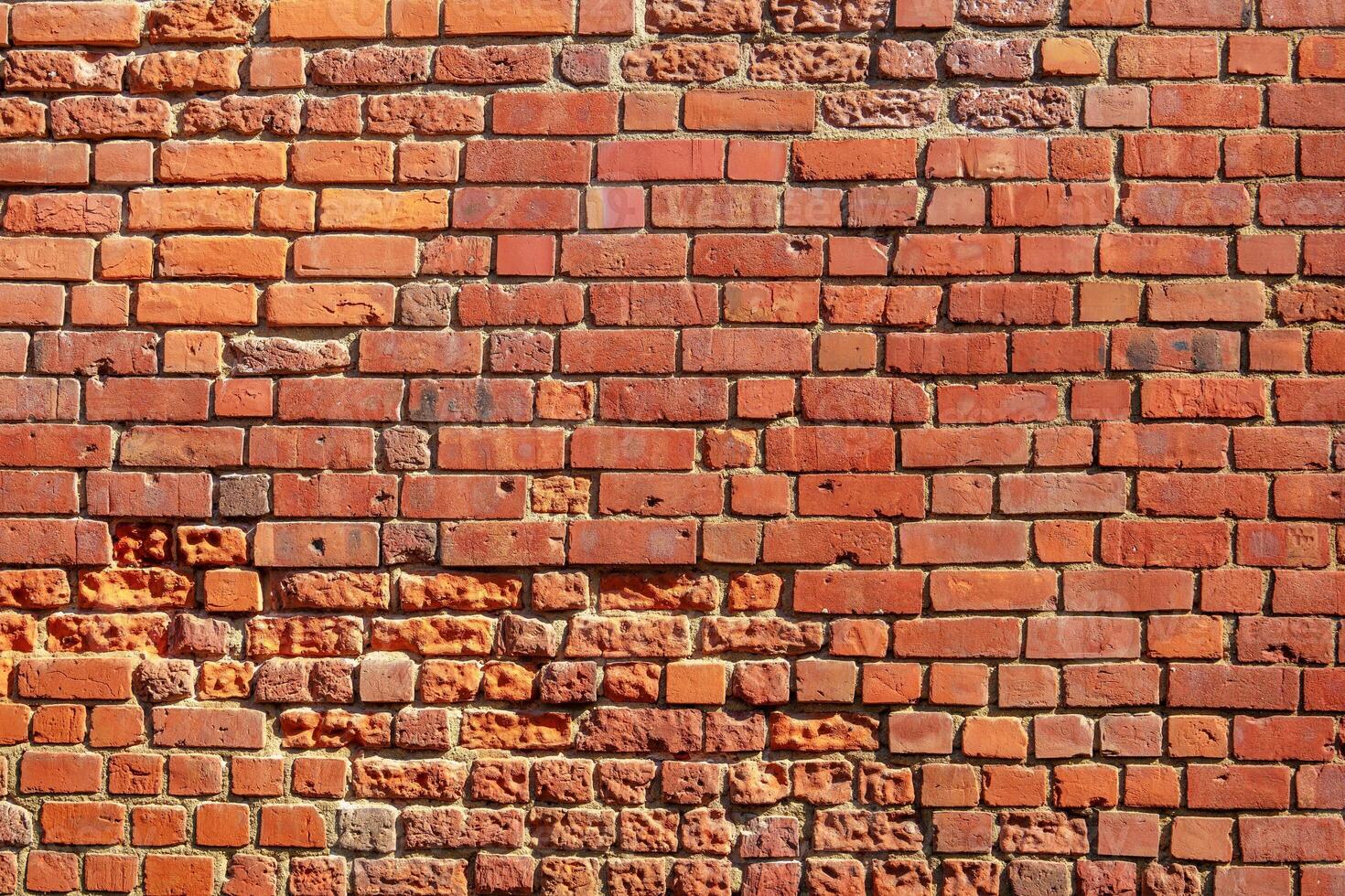 This image features a high-resolution texture of a classic red brick wall. The bricks are arranged in a neat stretcher bond pattern, showcasing their rough texture and vivid red color. photo