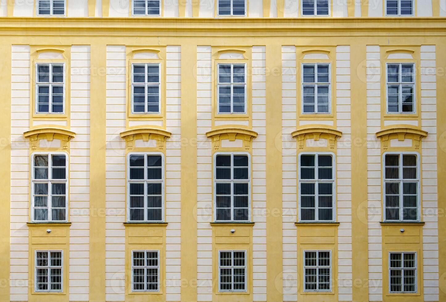 The historic European building facade features ornate yellow walls with barred windows and intricate architectural details. Perfect for history, travel, and architecture projects. photo