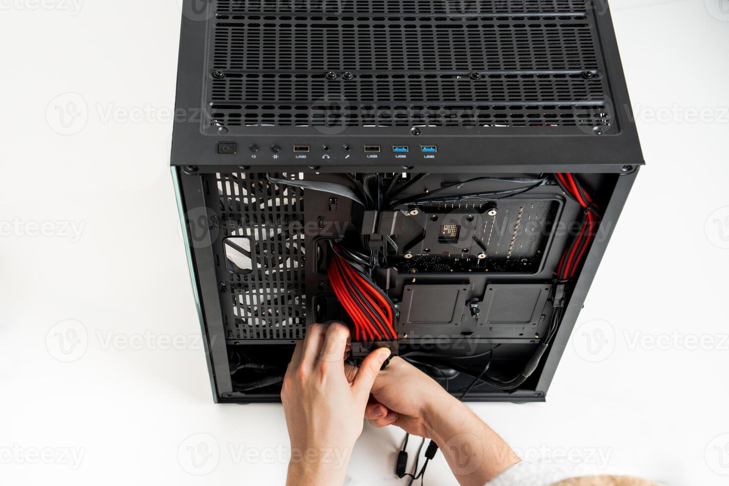 A focused individual is seen installing various hardware components into a sleek black computer case. The case is open, revealing the interior, while the persons hands adjust the components with precision. photo