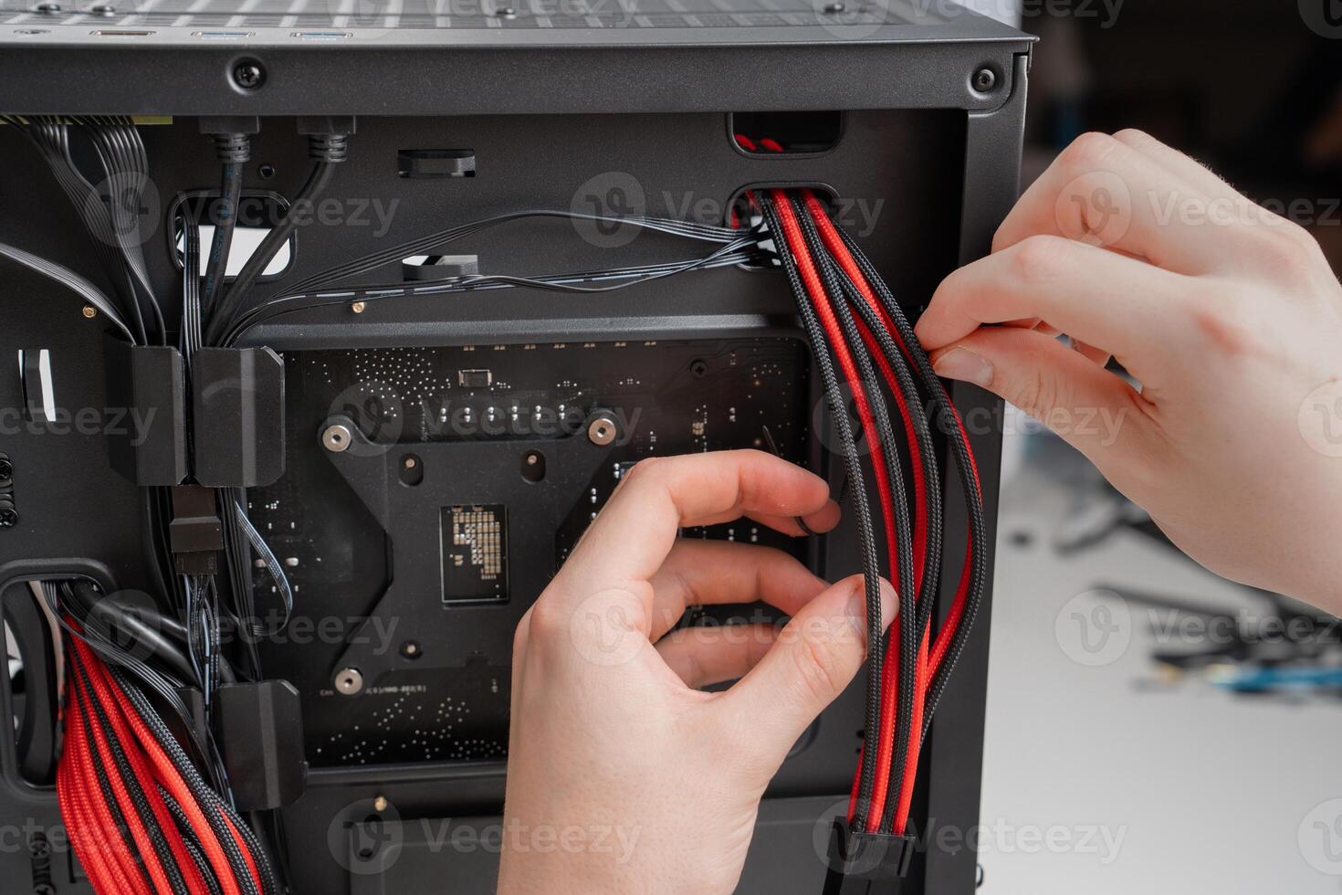 A black and red themed ATX mid-tower PC build with a tempered glass side panel and ARGB lighting. A hand holds the back panel open, showcasing the motherboard, CPU cooler, graphics card, and RAM. photo