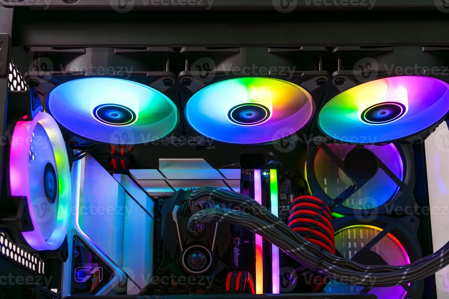 The image depicts an open black computer case featuring several cooling fans glowing in bright rainbow colors. The case has a tempered glass side panel, showcasing the fans arranged vertically. photo