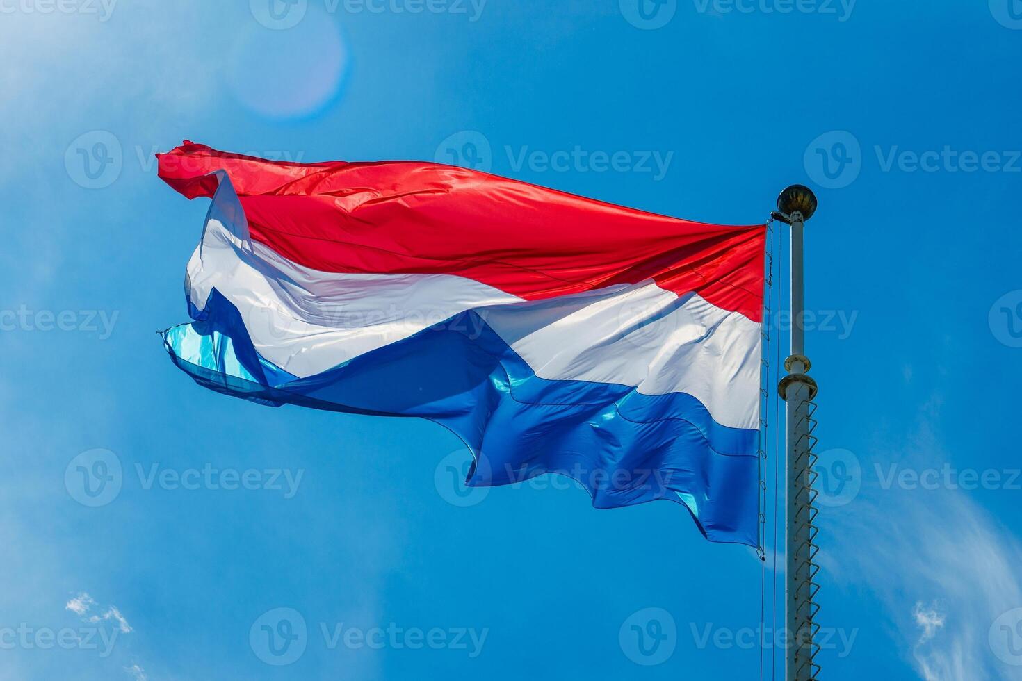 The Luxembourg flag, a vibrant tricolor of blue, white, and red, waves in the wind against a bright blue sky, representing the nations values of liberty, equality, and the spirit of fraternity. photo