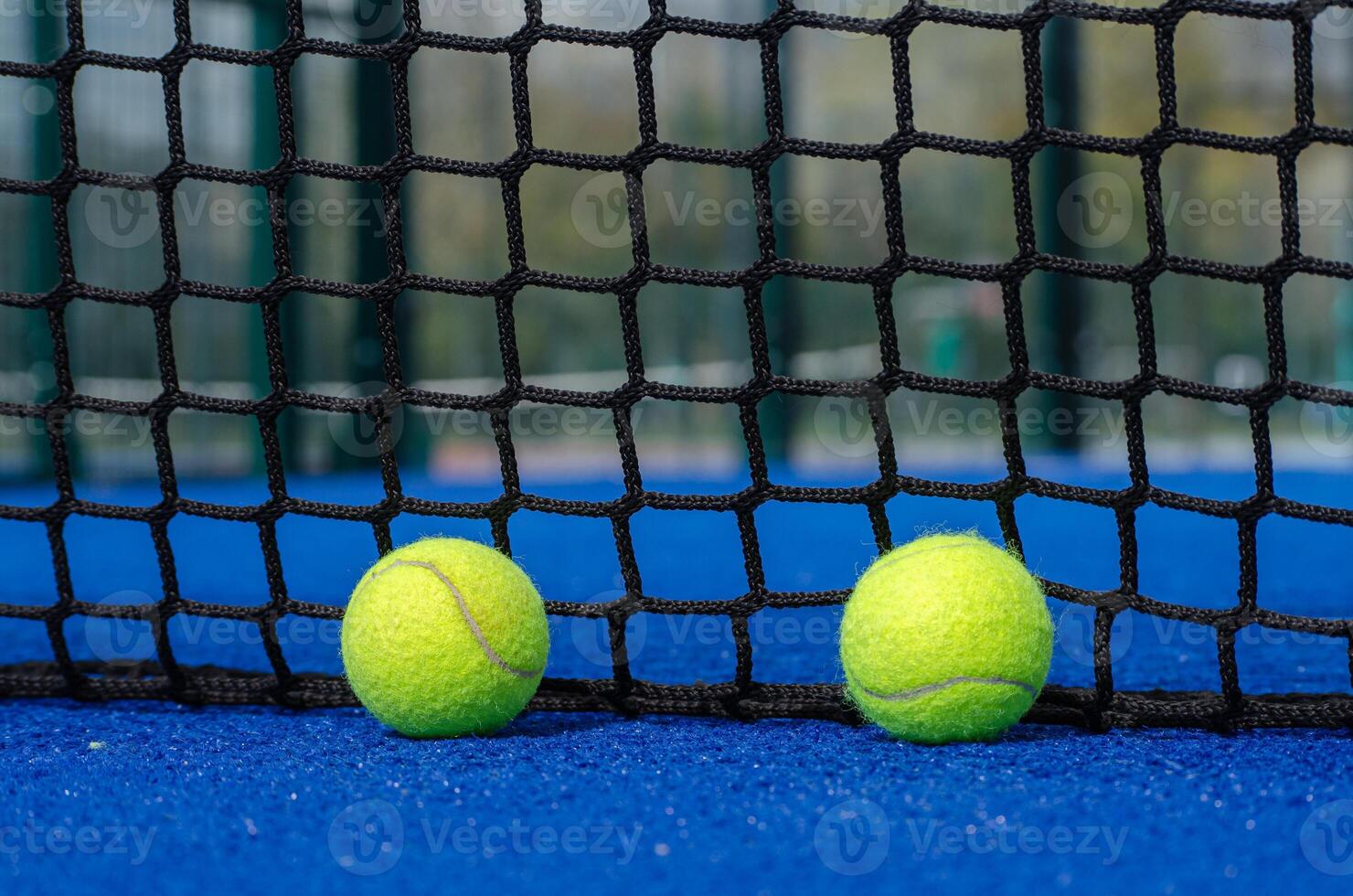 two paddle tennis balls over the service line and near the net of a blue paddle tennis court photo