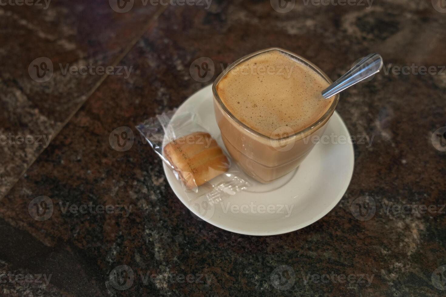 Coffee with milk in a crystal glass and a complimentary cookie in a Spanish coffee shop. Typical drink concept. photo
