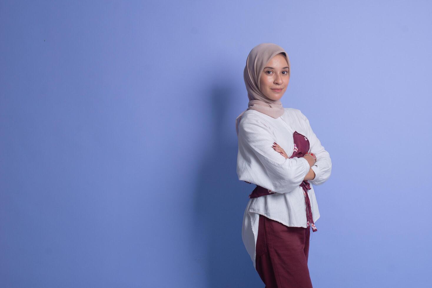 Young muslim woman standing with arms crossed against blue background photo
