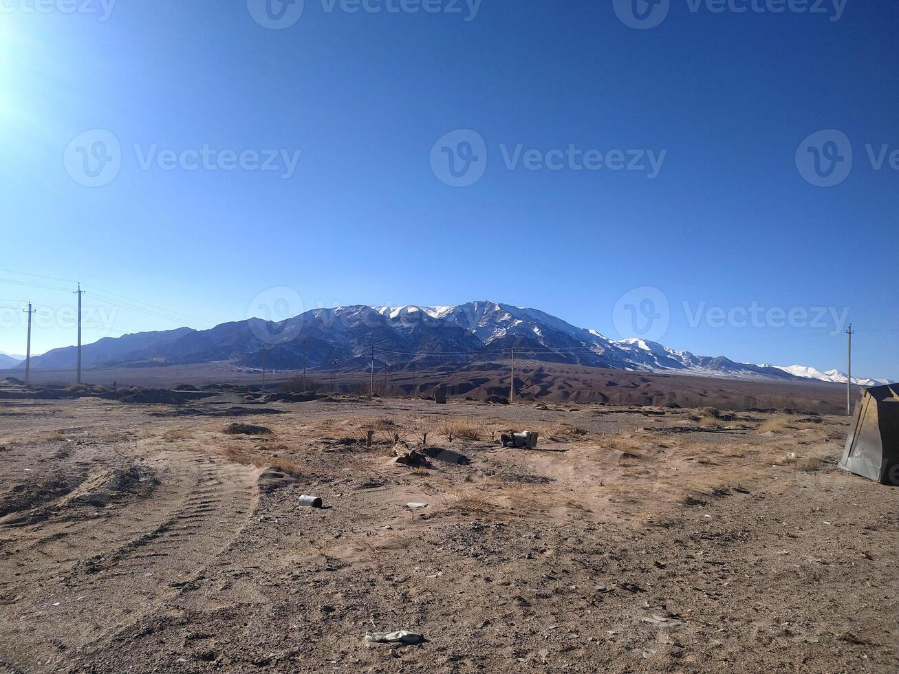 Serene landscape featuring majestic snow-capped mountains under a clear blue sky in a remote desert area during daylight hours photo
