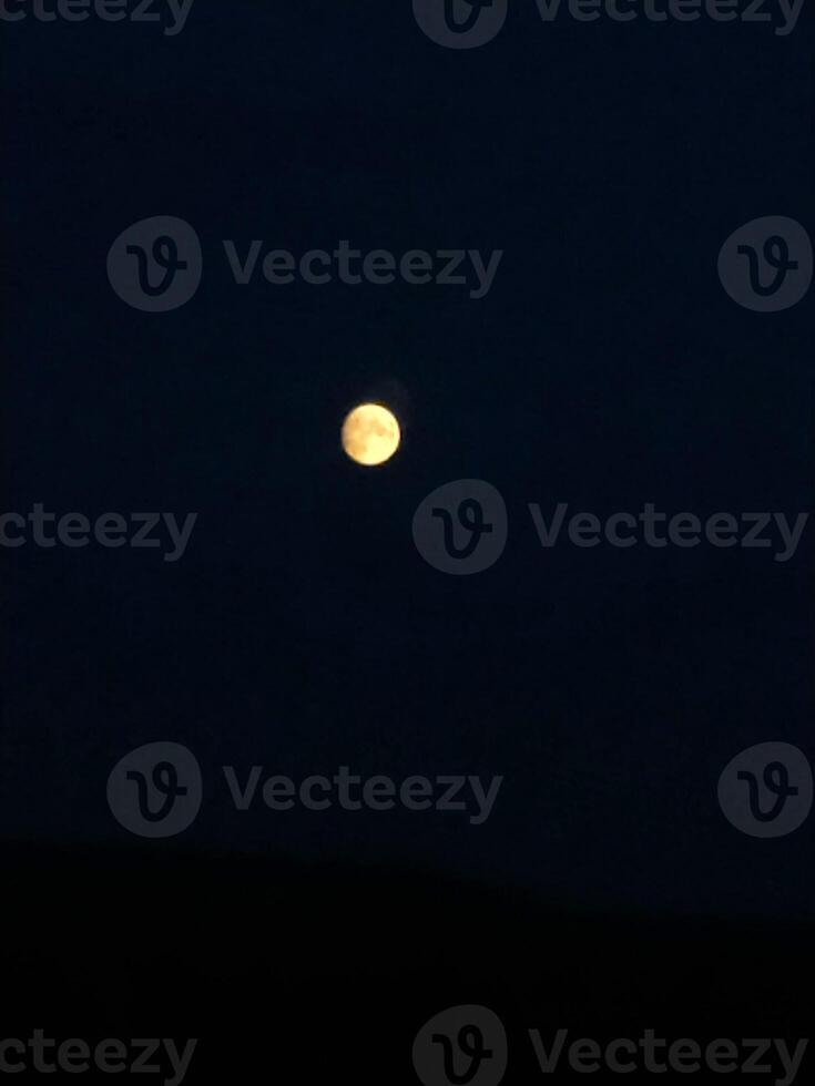 A bright full moon illuminates the dark night sky over a serene landscape, creating a magical atmosphere during a clear evening photo