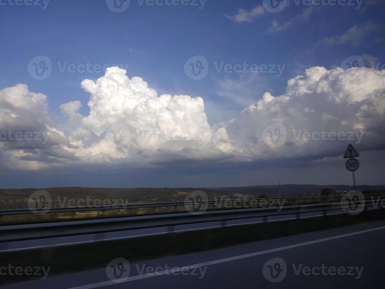 Majestic clouds drift lazily under a vibrant sky while a winding road leads into the serene landscape of a quiet countryside photo