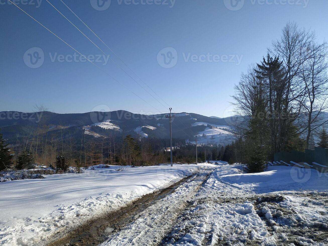 Snow-covered trail leading through mountains on a clear winter day with blue skies and distant peaks photo