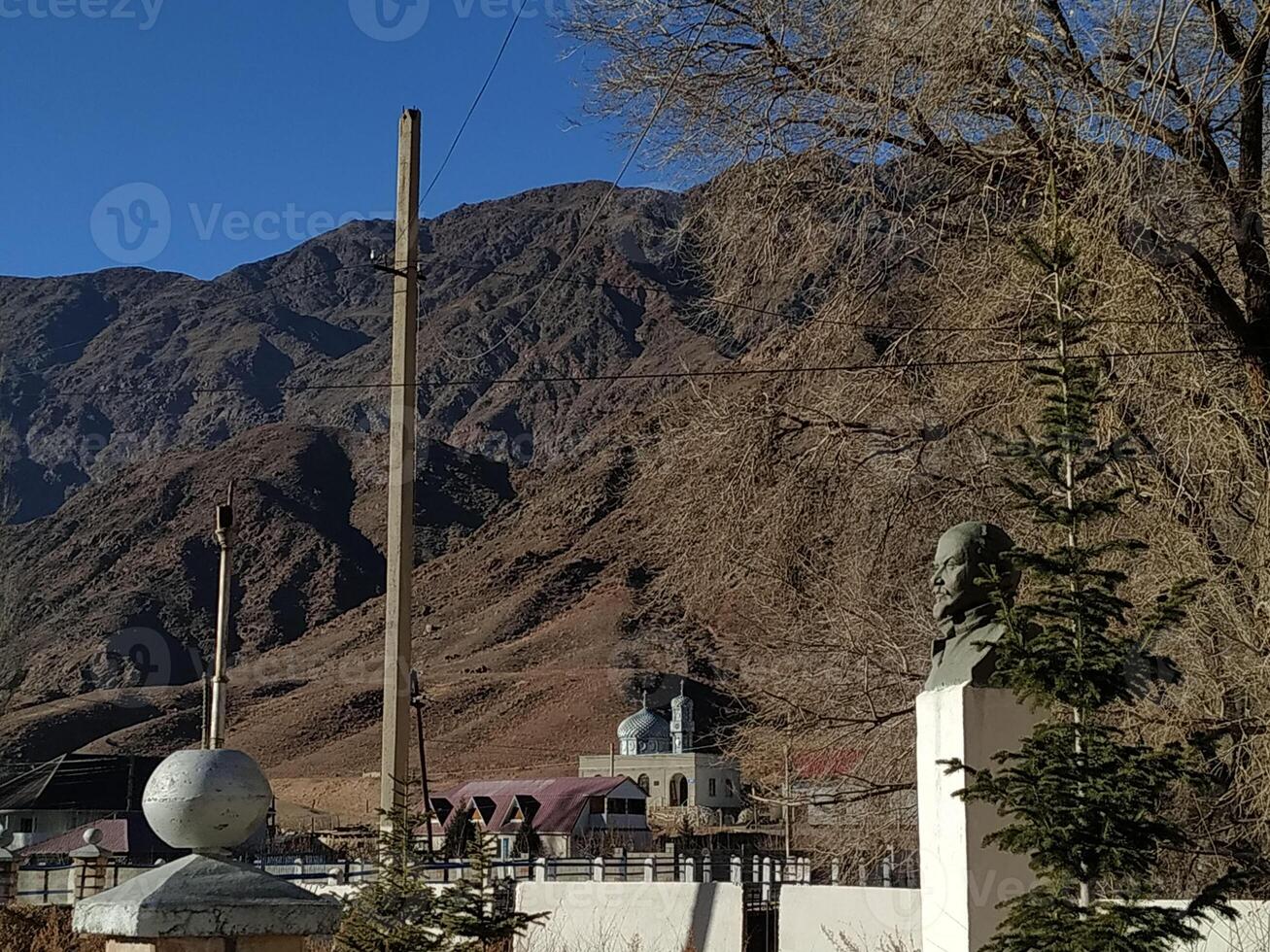 A tranquil afternoon view of imposing mountains framed by trees and historic statues in a remote village photo