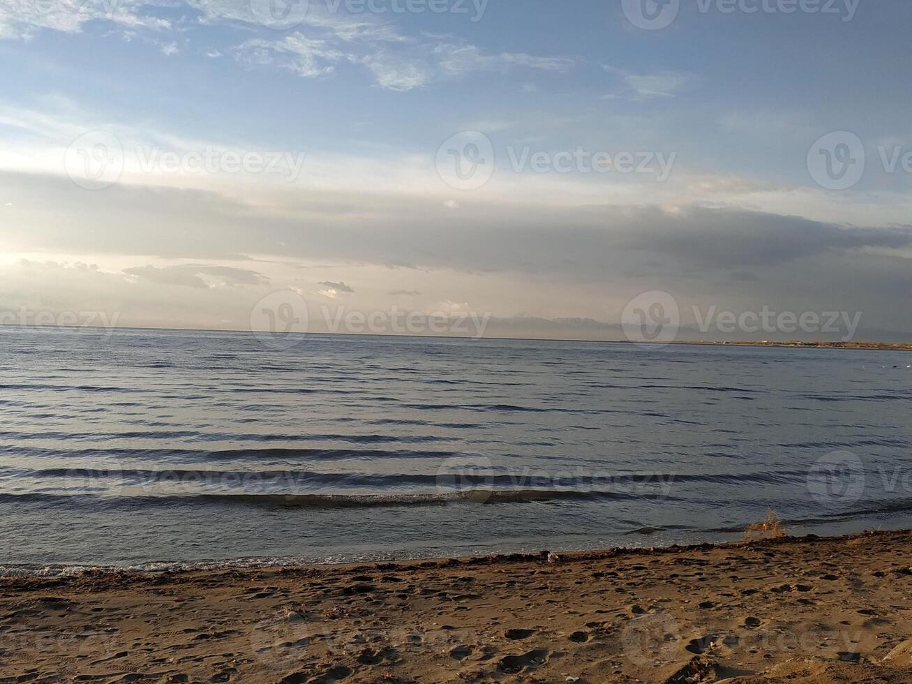 Tranquil shoreline at dusk with gentle waves lapping against the sandy beach under a vast, colorful sky photo