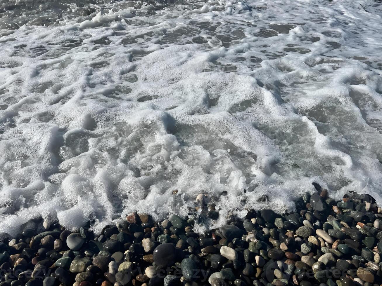 Ocean waves washing over a pebble-strewn shore with frothy sea foam in a serene coastal scene photo