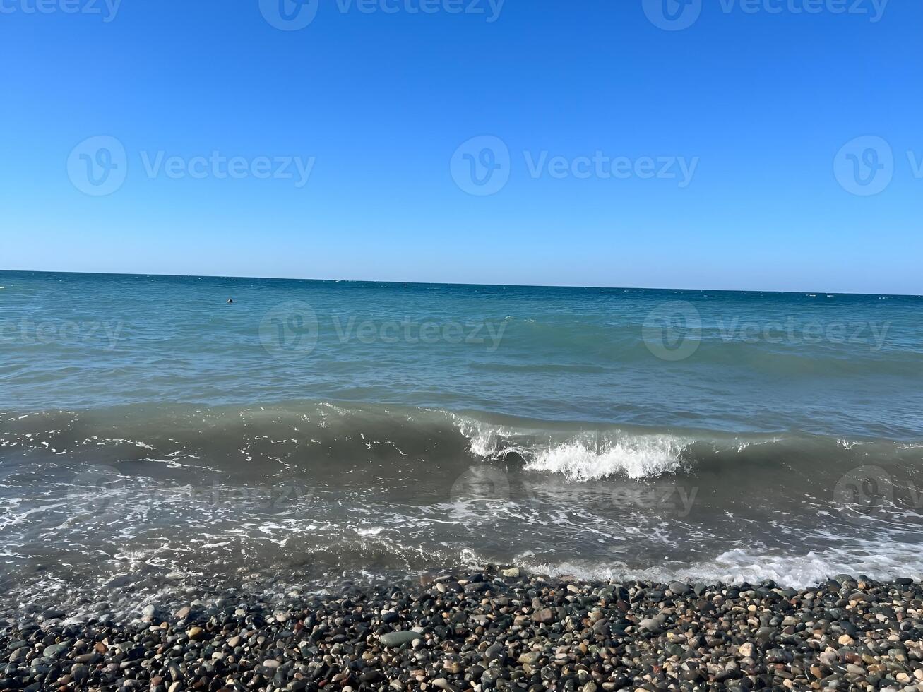 Peaceful coastal scene with gentle waves lapping onto a pebble beach under a clear blue sky photo