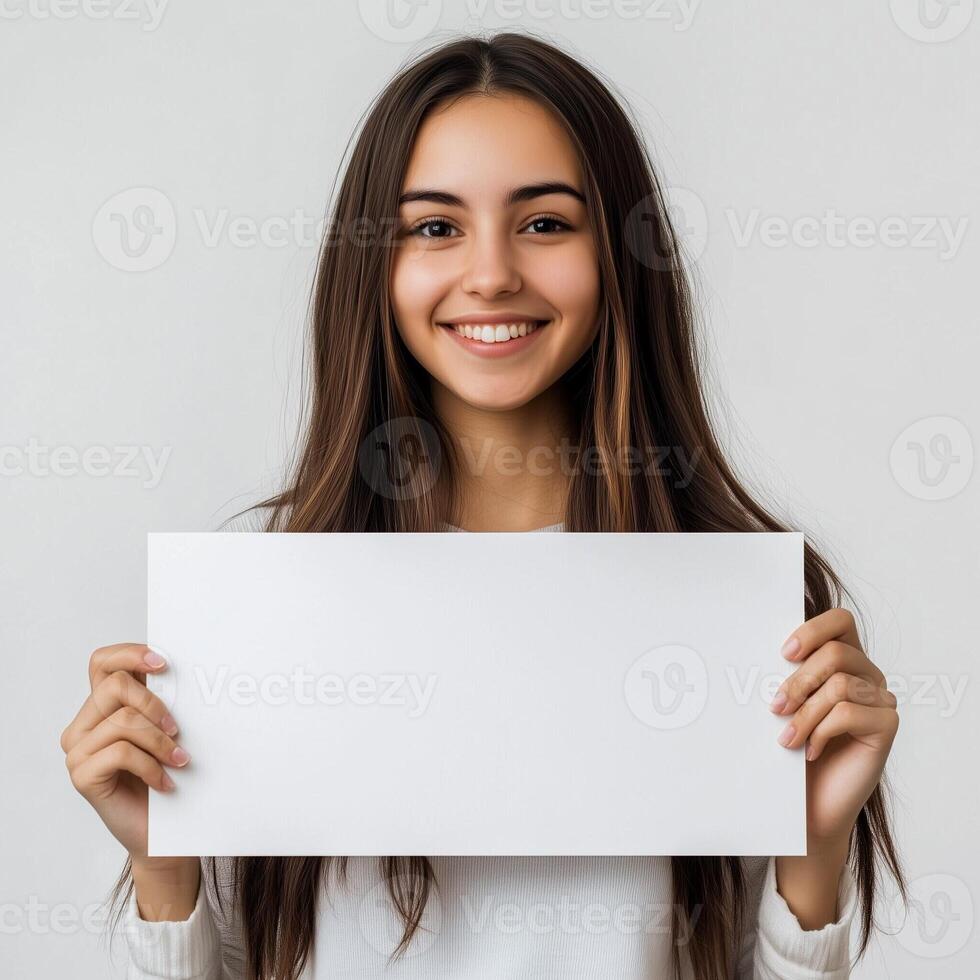 Smiling young woman holding blank white sign in front of her for advertisement or message in a minimalist background photo