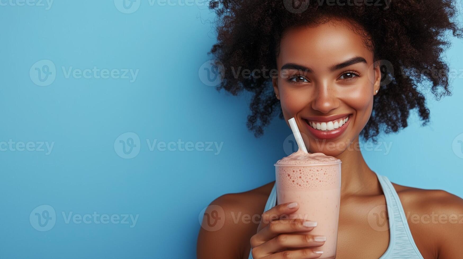 Smiling woman enjoying a refreshing smoothie while posing against a bright blue background in a healthy lifestyle concept photo