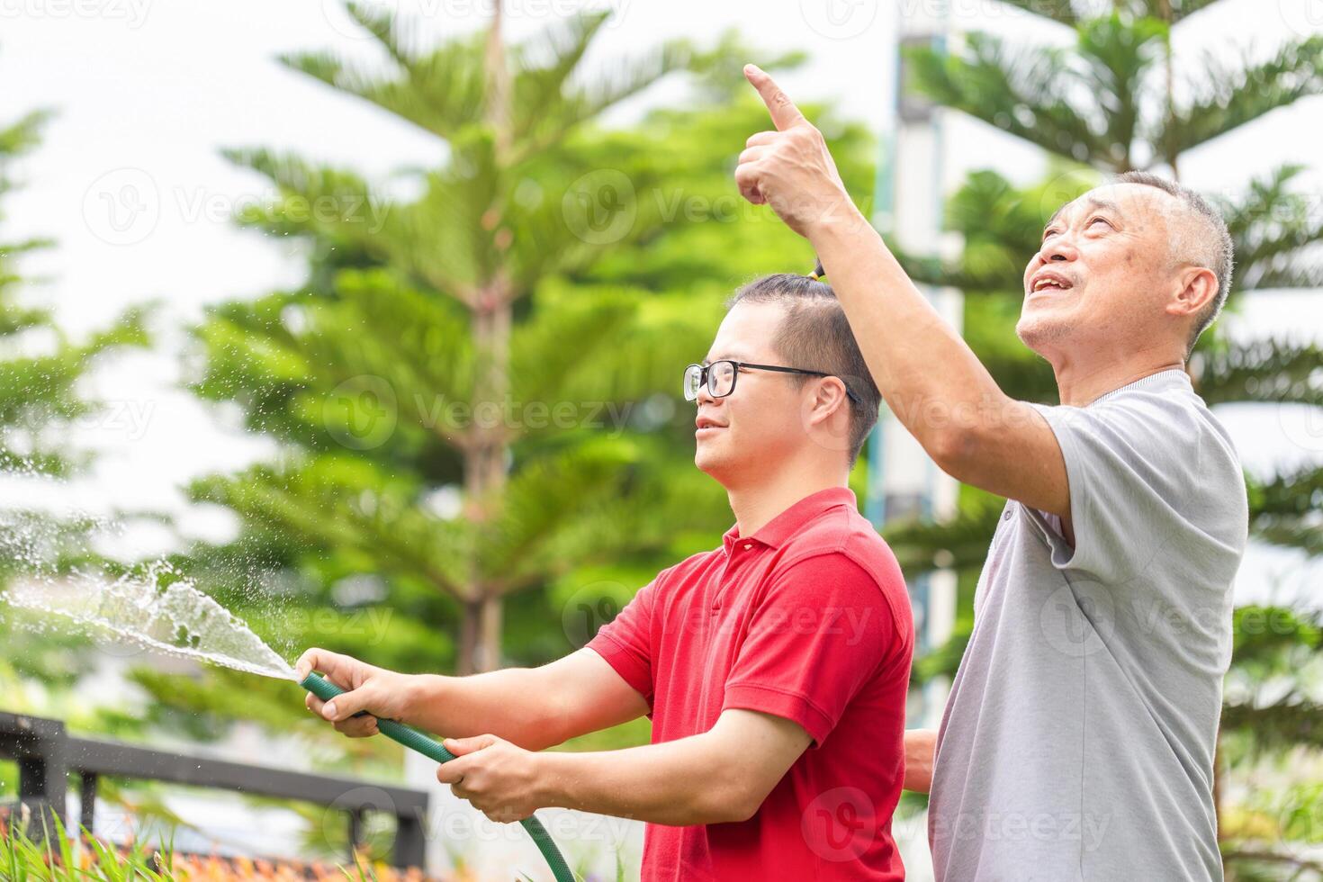 Cheerful grandfather with grandson working in the front yard garden, Senior man and grandson enjoying together are watering the plants with hose photo
