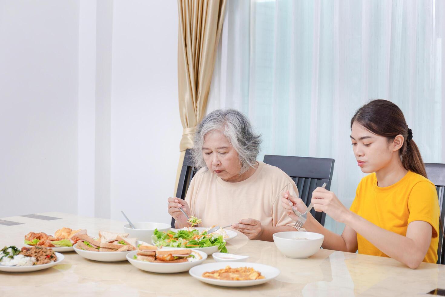 Mother and adult daughter eating meal together, Senior woman and daughter having breakfast in morning together photo