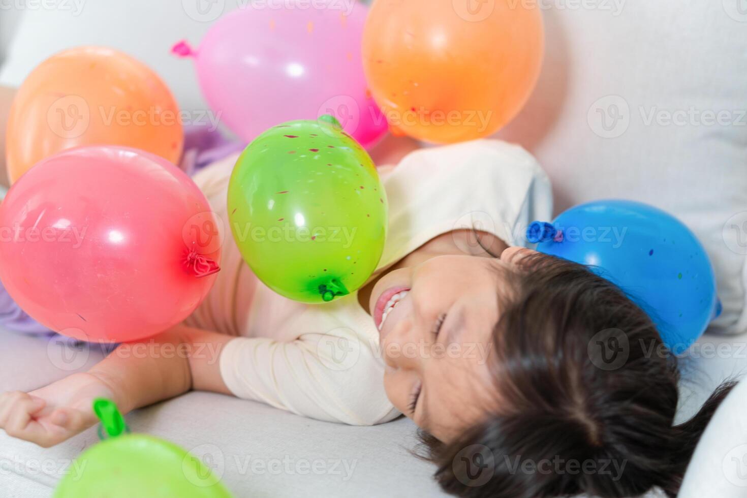 Asian kid girl with multicolor balloons, Cheerful girl playing air balls in living room photo