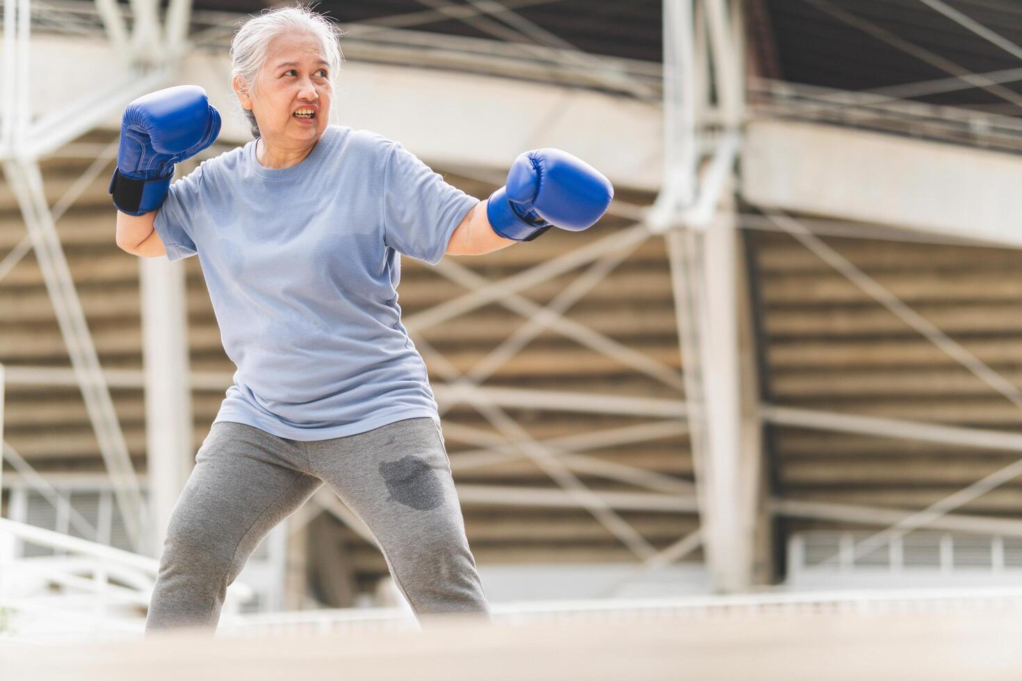 Senior Asian sportswoman boxing while working out on parking outdoors, Portrait of a senior mature woman exercising and stretching outdoor photo