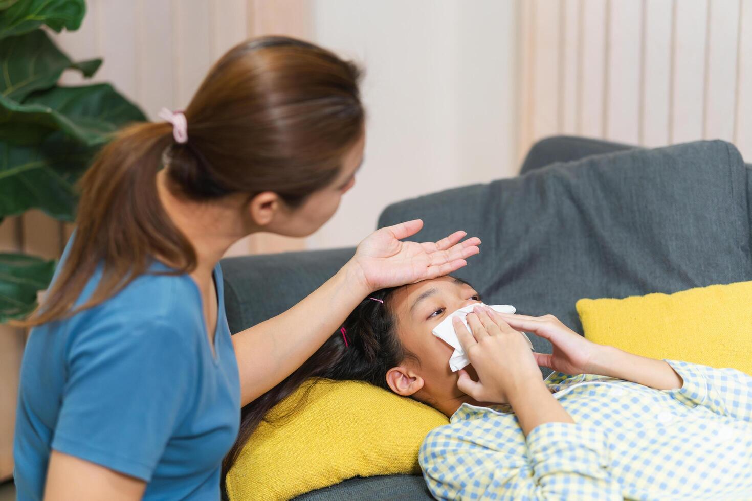 Asian mother is gently placing her hand on her child forehead to check for a fever photo