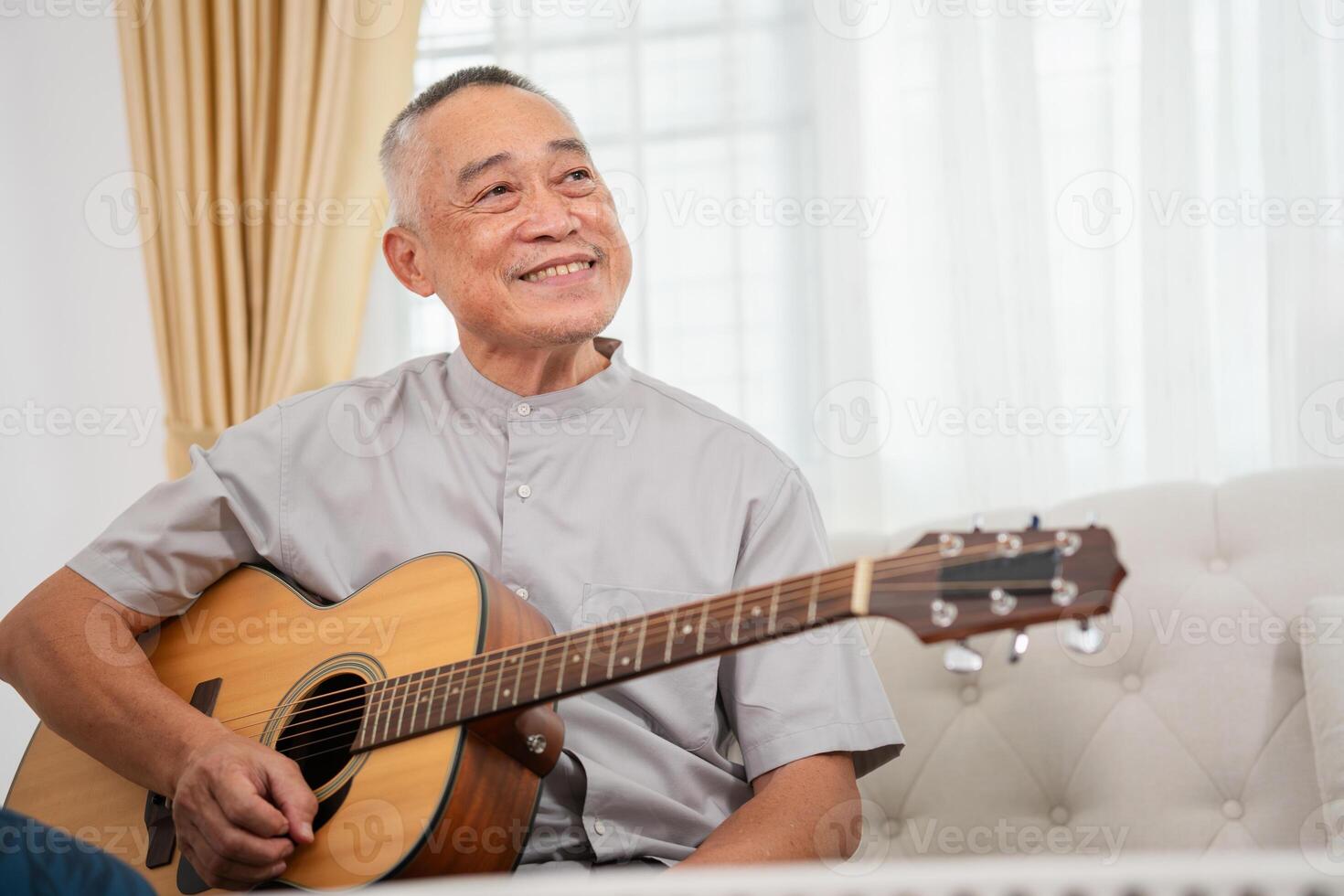 Asian senior man with acoustic guitar in living room, Man playing a guitar at home photo