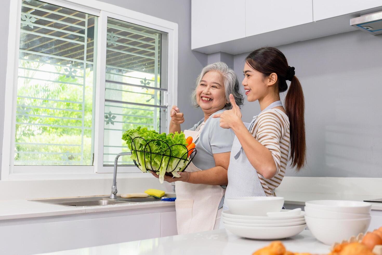 Cheerful senior asian mother and middle aged daughter cooking together at kitchen photo