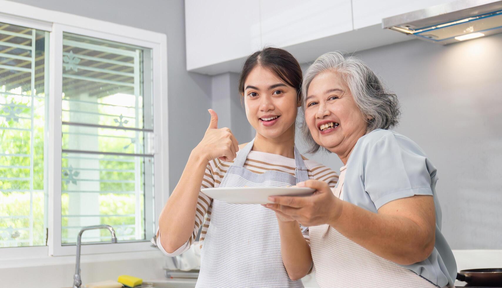 Middle aged daughter and senior mother cooking together at kitchen, Asian woman holding a plate for show your design photo
