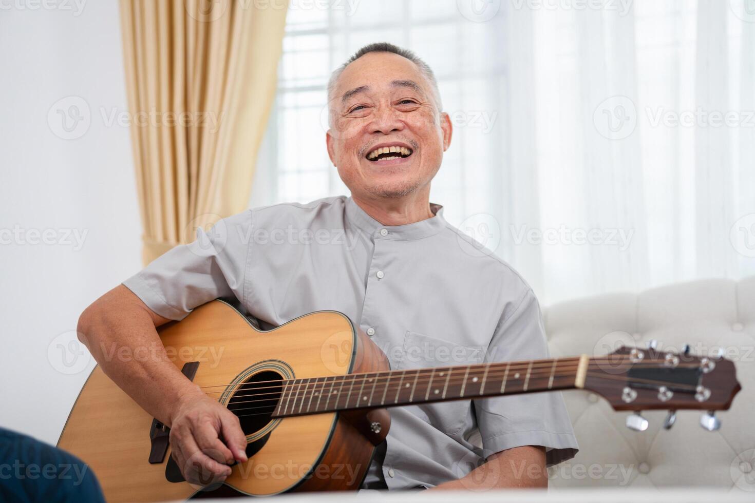 Cheerful Asian senior man with acoustic guitar in living room, Man playing a guitar at home photo