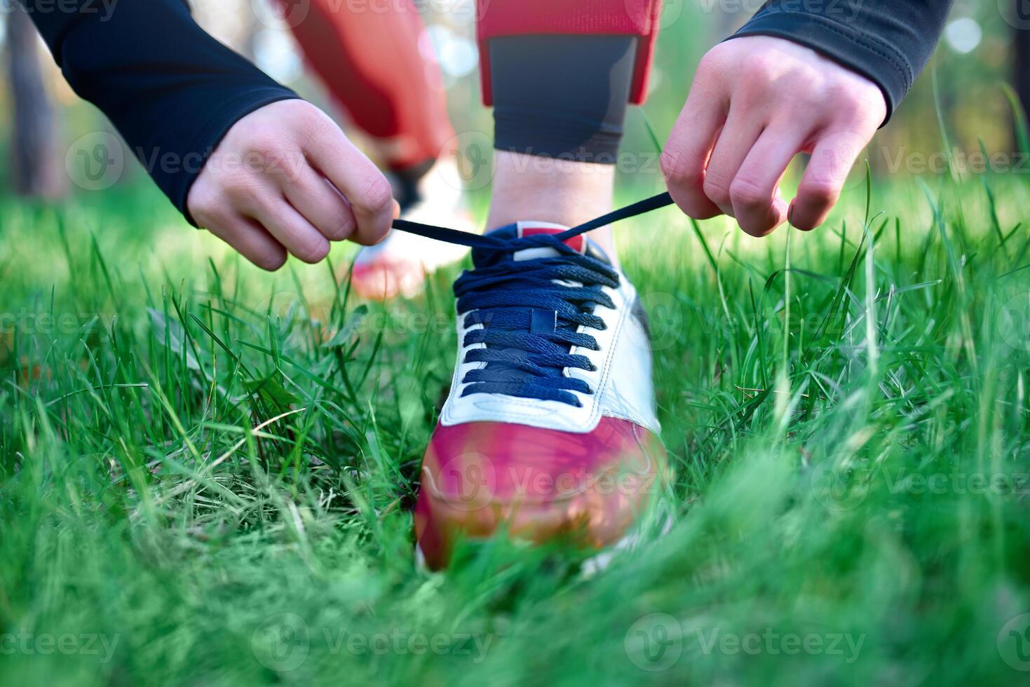 Person tying shoelaces on a red and white sneaker, preparing for an outdoor activity in a grassy area photo
