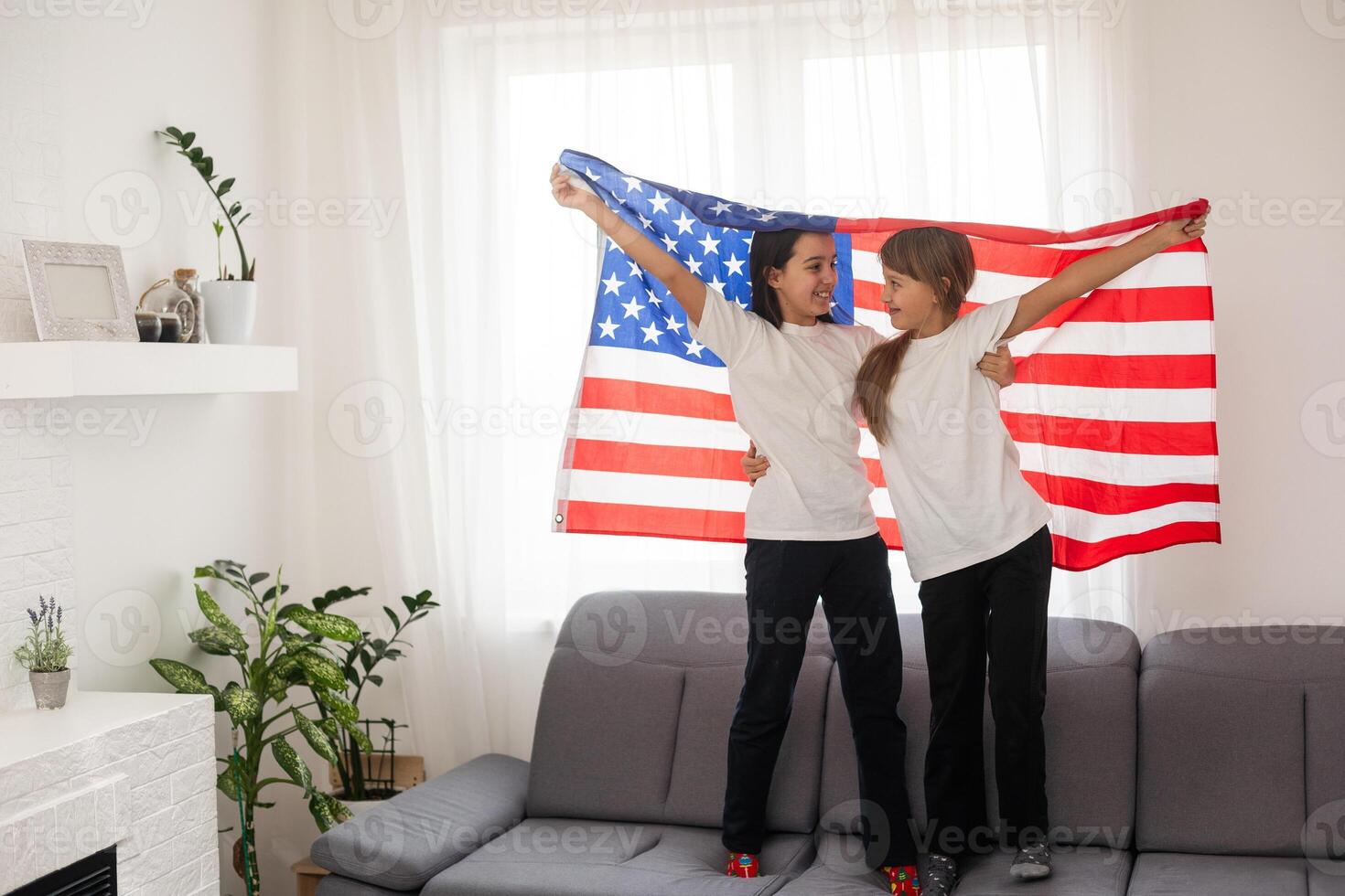 Brunette and blonde teenage girlfriends in white t-shirts holding american flag, energetic teenage friends spending time, friendship photo
