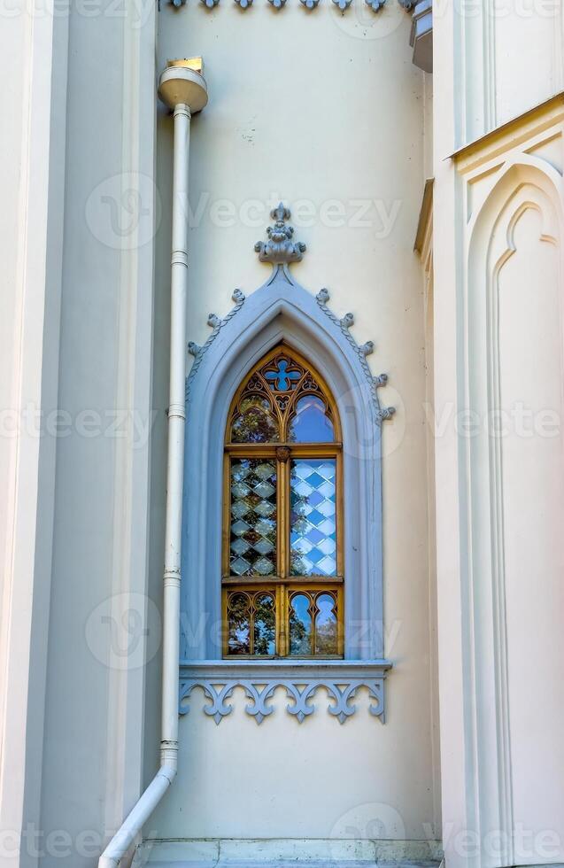 A series of pointed arched Gothic windows framed in gold with intricate lattice patterns adorn the exterior of a historic building. Captured in natural daylight, the windows reflect the surrounding photo