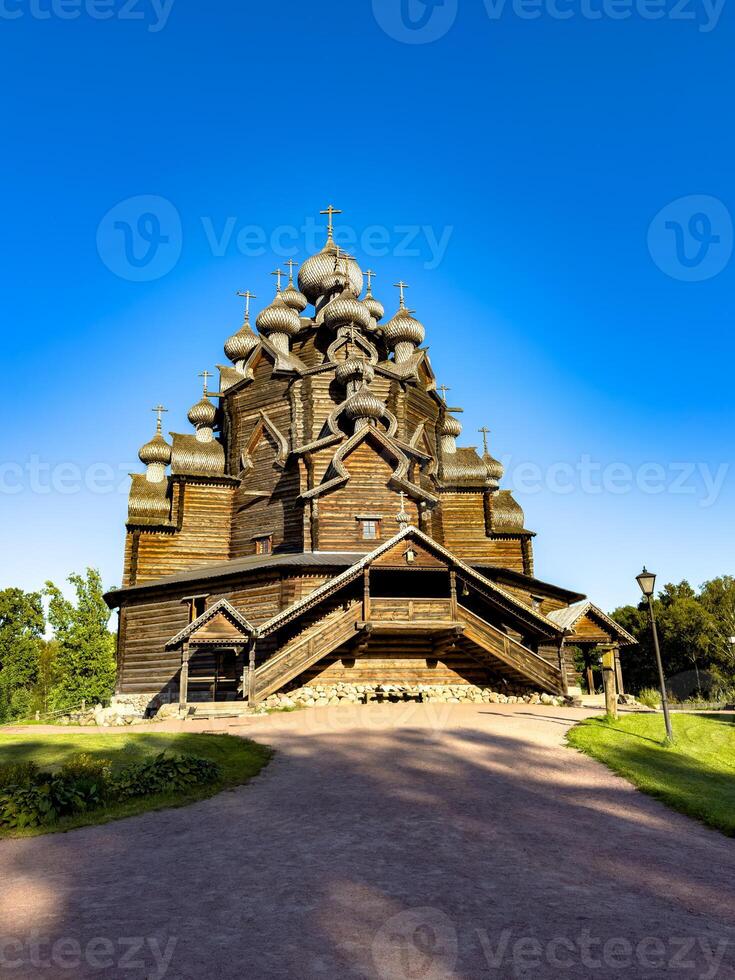 A traditional wooden Orthodox church with intricate onion domes, basking in the warm sunlight on a clear day. The rustic architecture stands against a vibrant blue sky, highlighting the cultural and photo