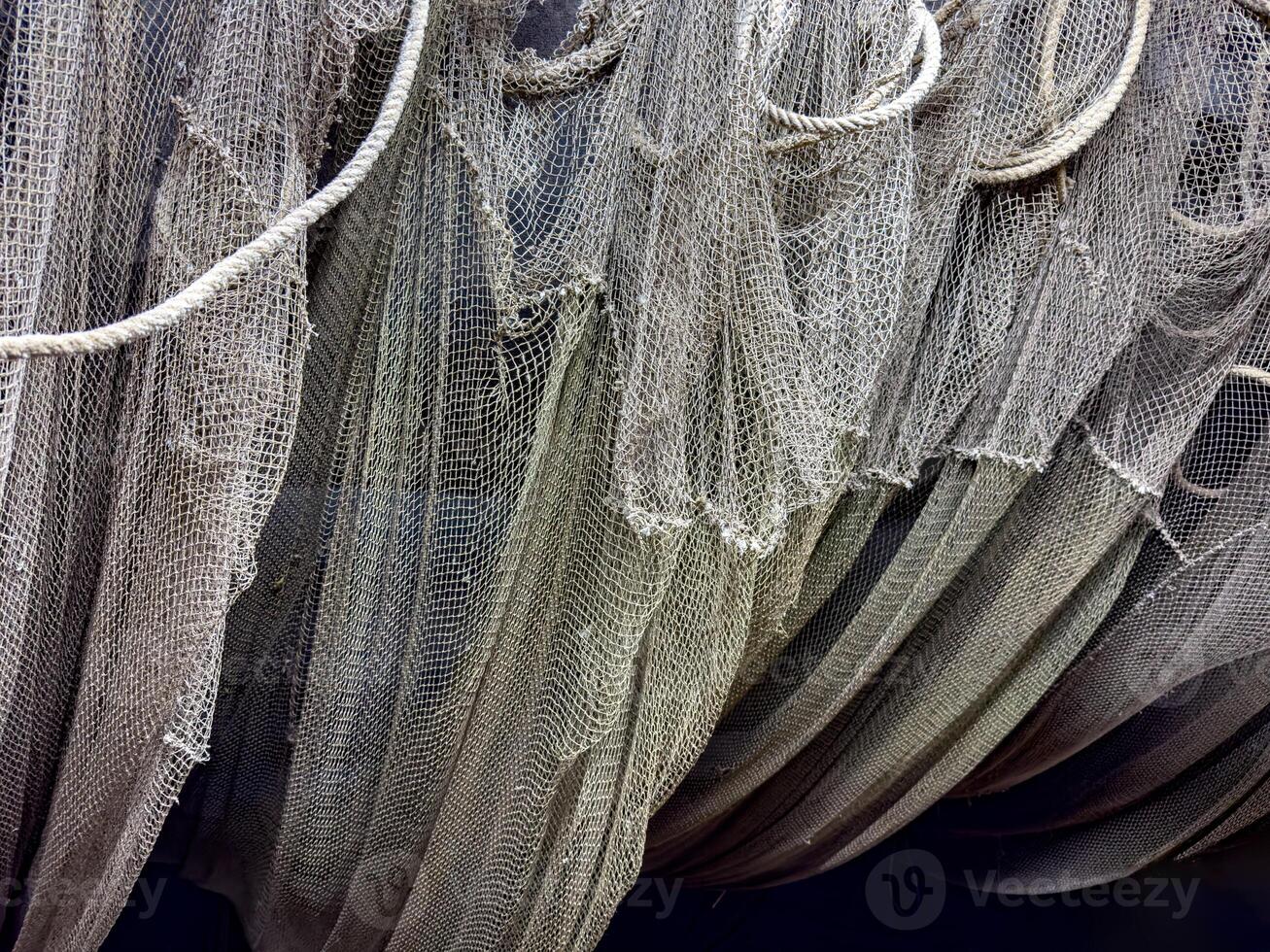 A detailed view of tangled fishing nets hanging from ropes, creating intricate layers of texture. The weathered appearance evokes the rugged life of fishermen and the maritime industry photo