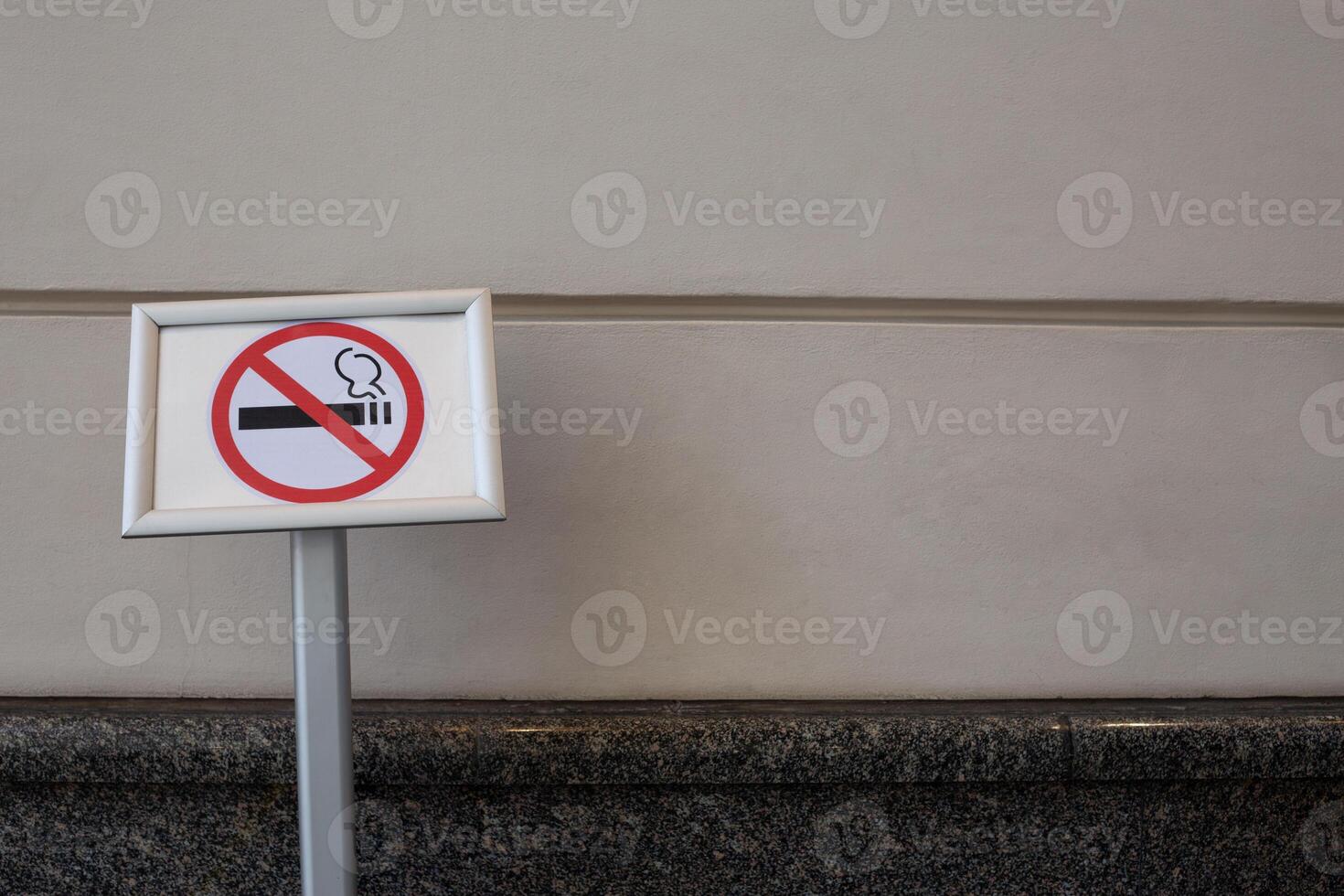 Sign prohibiting smoking on special pole near building, no smoking area against the background of wall photo