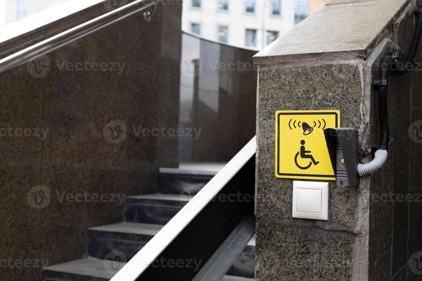 Wheelchair ramp with call button near stairs, yellow sign to indicate folding ramp for easy descent for persons with disabilities, accessible button and ramp equipment for the disabled on street photo