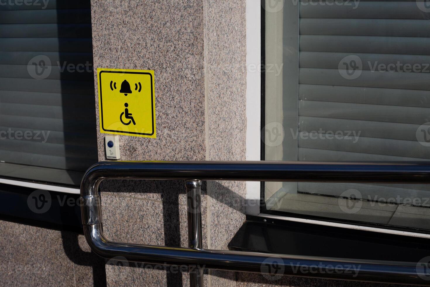 Hand rails to assist person in wheelchair next to handicap sign on wall and call button to assist person with disability, modern entrance to building with convenient ramp for people with disabilities photo