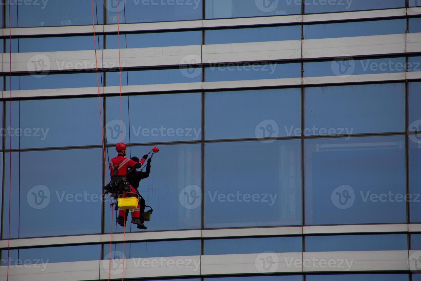 Climber sits on special safety bench and cleans glass windows of office skyscraper, cleaning the facade of building photo