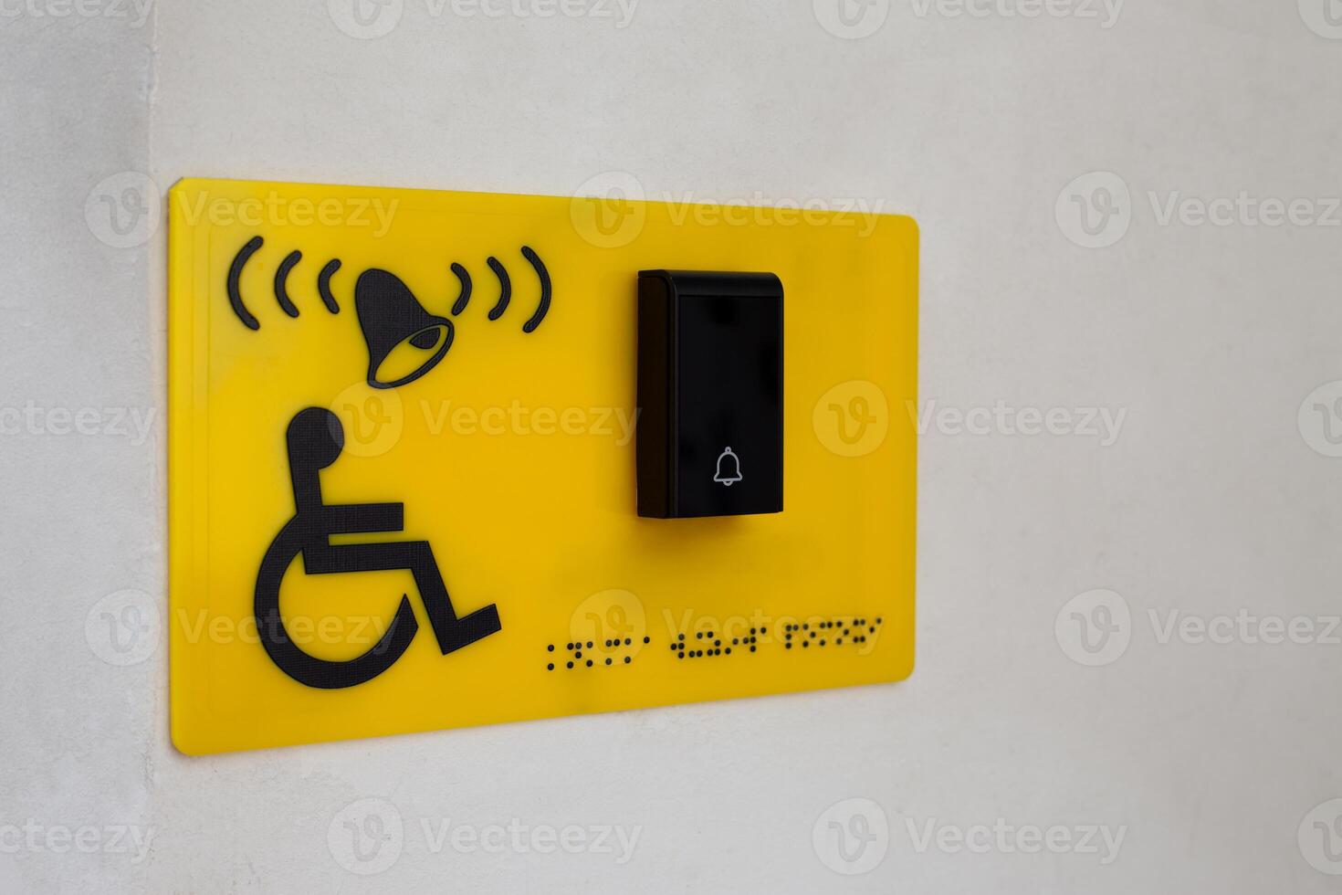 Yellow sign on wall of building with sign of person in wheelchair next to button to call help and braille text for blind people. Helping people with disabilities on the street in city, accessible environment photo