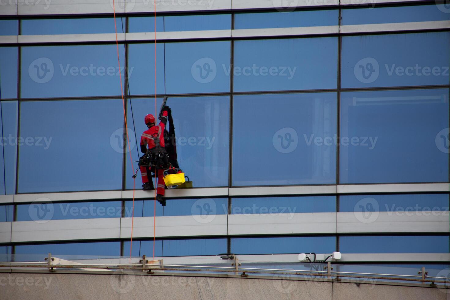 Heavy work with belay on ropes, climber rappels down the facade of building to wash windows, cleaning the facade of glass skyscraper photo