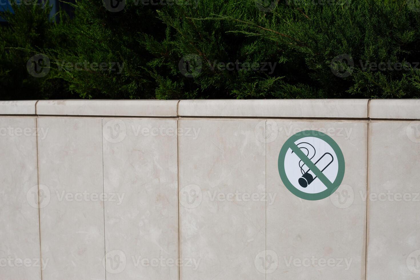Sticker on stone fence prohibiting smoking in park. Taking care of plants and preventing fire due to smoking in dangerous place, banning smoking in special area photo