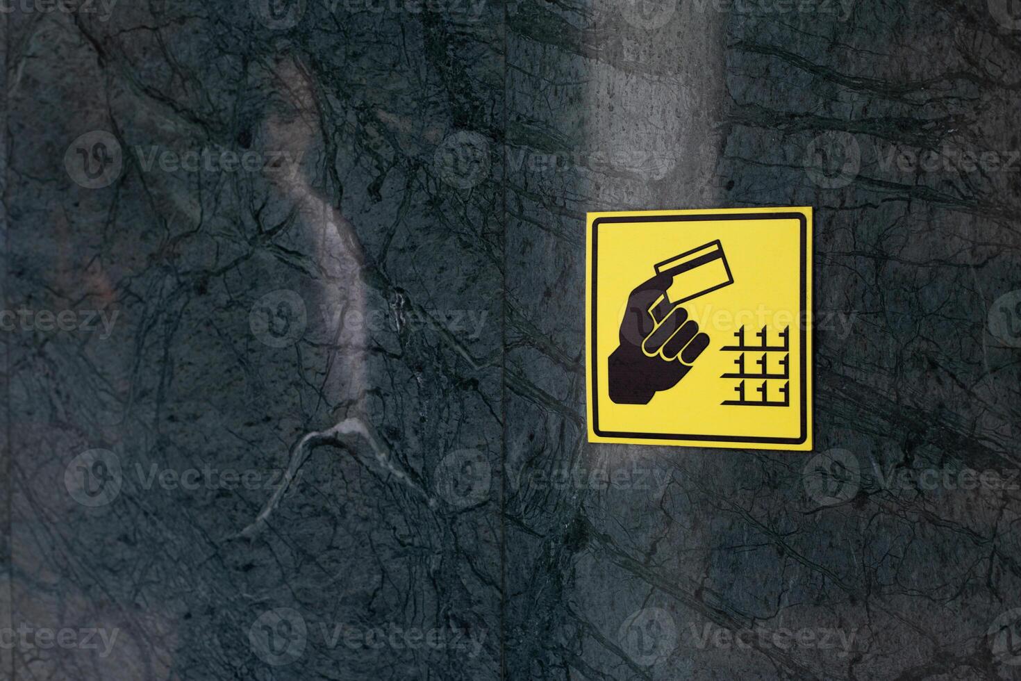 Yellow sign with black silhouette of hand with bank card in his hand near the ATM buttons. Sign on the wall to indicate where to place your card and pass photo
