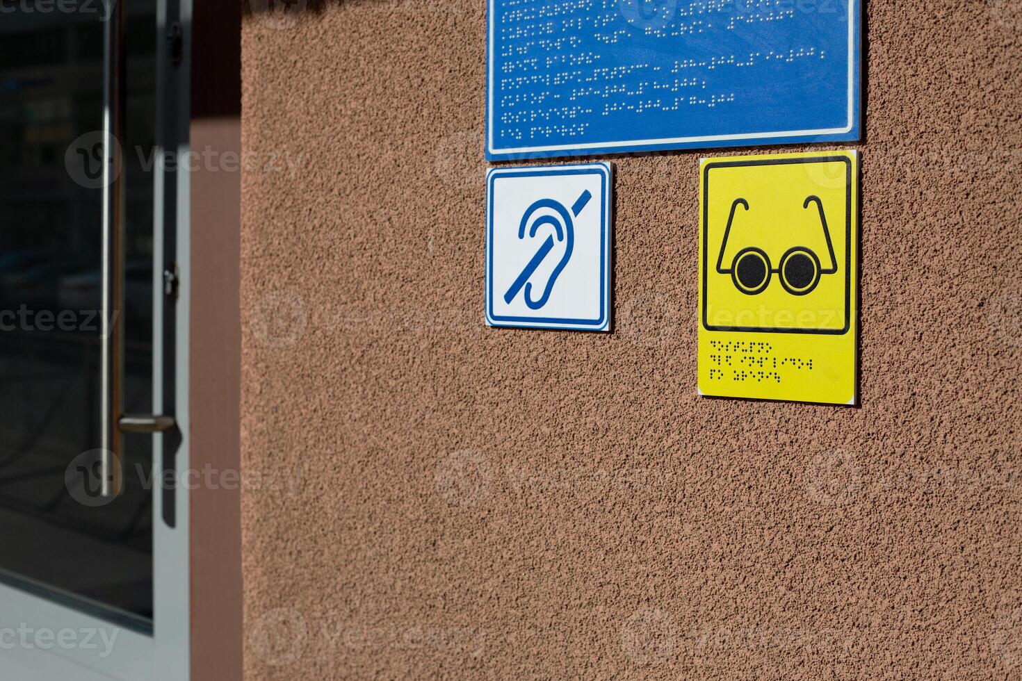 Social care conditions for people with disabilities, glasses and ear icon for blind and deaf people with information in braille text at entrance to building, accessible zone for disabled people photo